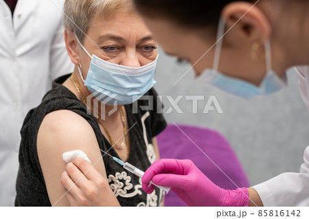 A nurse is making an vaccine to an elderly woman. The COVID vaccine19. A sterile doctor's office in a private clinic. A young medical intern looks at how to properly inject. A nurse is making an vaccine to an elderly woman. The COVID vaccine19. A sterile doctor's office in a private clinic. A young medical intern looks at how to properly inject. 85816142