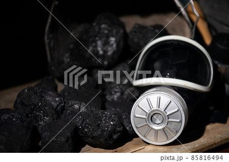 A gas mask with a filter lies on a wooden platform against a background of planks and black charcoal 85816494