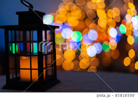 A darkened old hand lantern with a barely smoldering candle inside. On the second burn the background is blurred with Christmas tree lights and bokeh A darkened old hand lantern with a barely smoldering candle inside. On the second burn the background is blurred with Christmas tree lights and bokeh 85816500