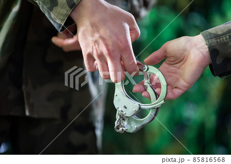 Soldiers pass metal handcuffs from hand to hand. Close-up view. Soldiers pass metal handcuffs from hand to hand. Close-up view. 85816568