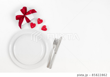 Valentines day or romantic dinner background. Festive romantic table setting with candles in the shape of hearts and a gift on a white background. 85822862