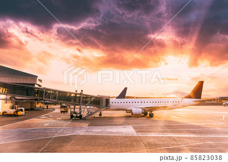 Aircraft Plane Airlines Stand At Airport Terminal In Early Morning. Sunset Sunrise Sun Sunshine Above Plane. Travel Trip Concept. Altered Sky. boarding terminal. beautiful dramatic sunlight light 85823038