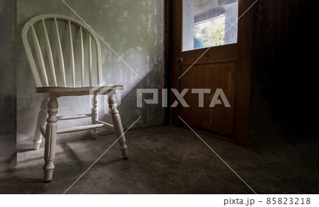 One white wooden vintage chair standing in an empty room under the light from the door. 85823218