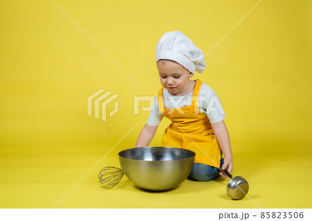 Boy in apron and chef's hat sitting on the floor with a bowl and whisk Boy in apron and chef's hat sitting on the floor with a bowl and whisk 85823506