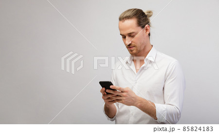 Young blonde bearded man texting message on smart phone over a white studio background with copy space 85824183