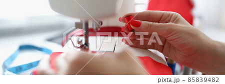 Female hands thread red thread into a sewing machine 85839482