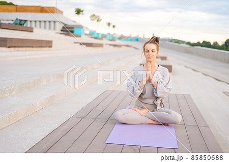 Portrait of attractive Caucasian young woman practicing yoga performing namaste pose with closed eyes outside in city park. Portrait of attractive Caucasian young woman practicing yoga performing namaste pose with closed eyes outside in city park. 85850688