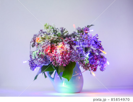 Beautiful bouquet of fragrant purple flowers in blue ceramics vase on light background. Syringa vulgaris or lilacs plant. 85854970