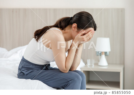 A woman sits in the bedroom and cries covering her face with her hands. A woman sits in the bedroom and cries covering her face with her hands. 85855050