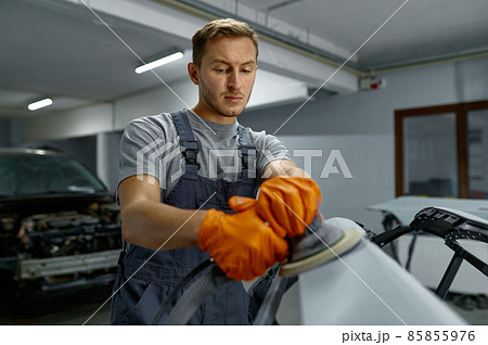 Serviceman polishing car body part in workshop 85855976