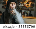 Young pretty woman in cap smoke an electronic cigarette at the vape shop. Hip-hop style. Closeup. 85856799