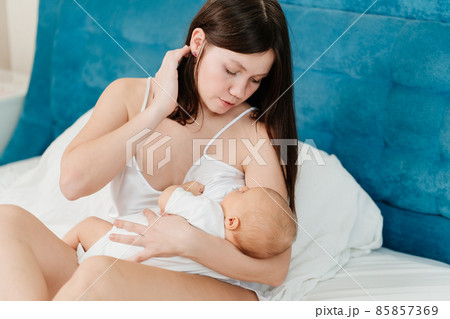 breastfeeding. mother in silk nightgown holds in his arms baby in bed. breastfeeding. mother in silk nightgown holds in his arms baby in bed. 85857369