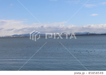 青空と雲と山と橋とビルのある街並みと水鳥のいる穏やかな湖面の琵琶湖の風景 85858549