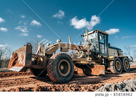 Road grader smoothing gravel surface for new road. Scraper leveling ground, working at construction 85858962