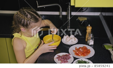 Smart girl learning to cook. Young mistress children to cook a Neapolitan egg fried omelette from salame affumicato sausage. 85859241