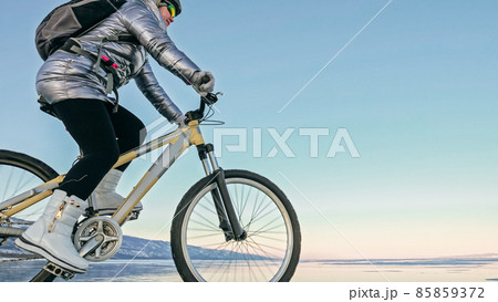 Woman is riding bicycle on the ice. Tires on bike are covered wi Woman is riding bicycle on the ice. Tires on bike are covered wi 85859372