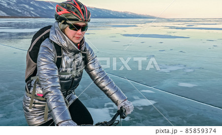 Woman is riding bicycle on the ice. Tires on bike are covered wi 85859374