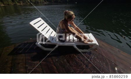 Woman lie on a sunbed in sunglasses and a boho silk shawl. Girl rest on a flood wood underwater pier. The pavement is covered with water in the lake. 85860259