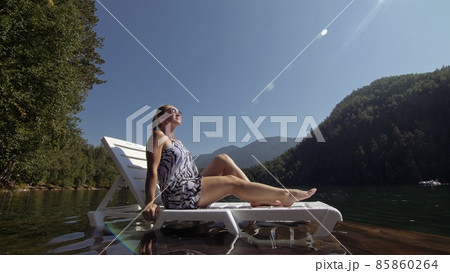Woman lie on a sunbed in sunglasses and a boho silk shawl. Girl rest on a flood wood underwater pier. The pavement is covered with water in the lake. Woman lie on a sunbed in sunglasses and a boho silk shawl. Girl rest on a flood wood underwater pier. The pavement is covered with water in the lake. 85860264