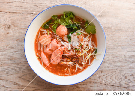 Red soup noodle pork with red roasted pork and bean sprout vegetable in soup bowl on wooden table, top view Thai and China Asian food 85862086