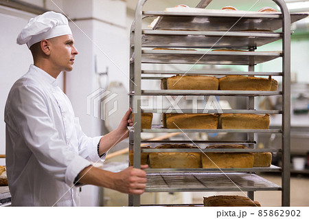 Male baker carrying rack trolley with bread 85862902