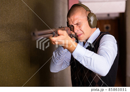 Focused man aiming shotgun at target in shooting range Focused man aiming shotgun at target in shooting range 85863031