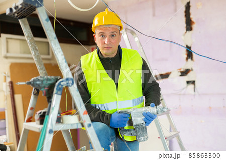 Repair man with drill standing in apartment 85863300