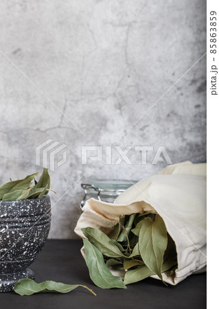 Food background with copy space. Dried bay leaf in a mortar, in a jar, in a linen cloth bag on the countertop. Mortar and pestle close-up. Proper storage and grinding of spices Food background with copy space. Dried bay leaf in a mortar, in a jar, in a linen cloth bag on the countertop. Mortar and pestle close-up. Proper storage and grinding of spices 85863859