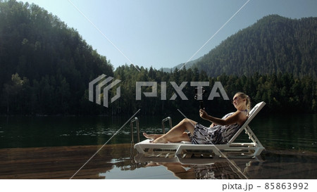 Woman shooting on handheld film gimbal stabilization for smartphone. Girl lie sunbed on pier make selfie. Blogger broadcast video vlogging. 85863992