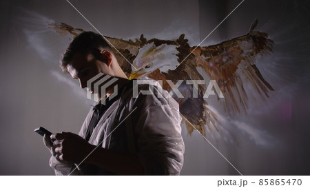 Artist designer draws an eagle on wall. Craftsman decorator paints picture with acrylic oil color looking at sketch in phone. Dark magic cinematic. 85865470