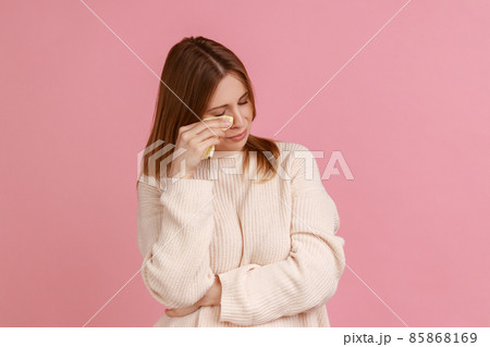 Portrait of blond woman frowning, wiping tears crying, feeling desperate hopeless, coping lonely in emotional stress, wearing white sweater. Indoor studio shot isolated on pink background. Portrait of blond woman frowning, wiping tears crying, feeling desperate hopeless, coping lonely in emotional stress, wearing white sweater. Indoor studio shot isolated on pink background. 85868169