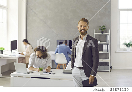 Portrait of smiling young Caucasian businessman stand in modern coworking office, employees on background. Happy successful male CEO or boss show leadership at workplace. Employment concept. Portrait of smiling young Caucasian businessman stand in modern coworking office, employees on background. Happy successful male CEO or boss show leadership at workplace. Employment concept. 85871139