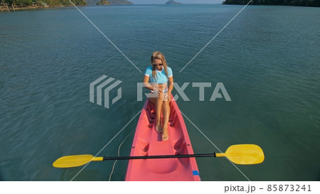 Pretty slim woman in elegant swimsuit lies in pink plastic kayak drifting on azure ocean at exotic resort upper view. 85873241