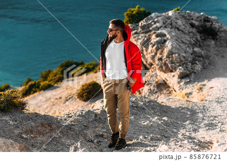 Portrait of a brutal bearded man in a red jacket by the sea. Male portrait on the background of a seascape. A traveler on the background of the sea coast. A man in a jacket at sunset 85876721