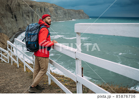 A man with a backpack on the background of the sea. Portrait of a man in tourist gear on the background of the sea. The concept of travel and an active lifestyle. A male tourist on the seashore A man with a backpack on the background of the sea. Portrait of a man in tourist gear on the background of the sea. The concept of travel and an active lifestyle. A male tourist on the seashore 85876736