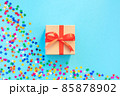 Gift box with a red bow on a blue background with multicolored stars of confetti. Flat lay composition for birthday or holiday. 85878902