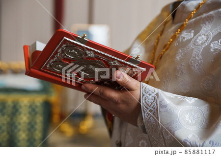 The priest reads the Bible during the ceremony. Orthodox Church. Christianity. Festive interior decoration with burning candles and icon. The ceremony of infant baptism. Baptismal font. 85881117