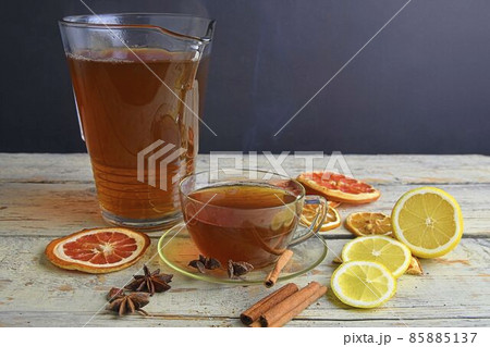 Glass cup of black tea with cinnamon sticks, anise star, lemon and dried fruit on white wooden table background. Jug of black tea. Large copy space. Black background empty space for text Glass cup of black tea with cinnamon sticks, anise star, lemon and dried fruit on white wooden table background. Jug of black tea. Large copy space. Black background empty space for text 85885137