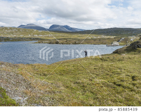 Fisherman, angler figure at northern landscape, tundra in Swedish Lapland with blue artic lake, green hills and mountains. Fishing at Padjelantaleden hiking trail. Summer day, blue sky, white clouds Fisherman, angler figure at northern landscape, tundra in Swedish Lapland with blue artic lake, green hills and mountains. Fishing at Padjelantaleden hiking trail. Summer day, blue sky, white clouds 85885439