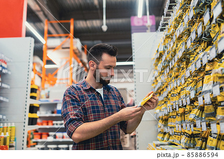a man chooses a product in a building materials store next to a showcase with self-tapping screws a man chooses a product in a building materials store next to a showcase with self-tapping screws 85886594
