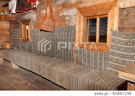 A fragment of the interior of the living room of an old Ukrainian rural hut with windows and a wooden bench along the perimeter of the room. A fragment of the interior of the living room of an old Ukrainian rural hut with windows and a wooden bench along the perimeter of the room. 85887296
