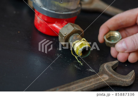 Man's hand is holding a brass plug in front of the water meter and wrenches. Man's hand is holding a brass plug in front of the water meter and wrenches. 85887336