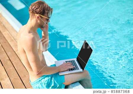 Young man at the swimming pool working on a laptop Young man at the swimming pool working on a laptop 85887368