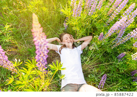 Happy teenage girl smiling outdoor. Beautiful young teen woman resting lying on summer field with blooming wild flowers green background. Free happy kid relaxing and enjoying nature 85887422