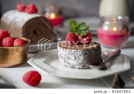 Chocolate roll cake or swiss dessert cake with raspberries. Romantic mood with candles. 85887803