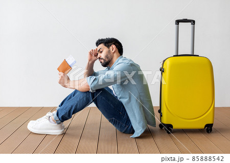 Upset arab man with passport and plane tickets leaning on suitcase, missed his vacation because of COVID-19 pandemic Upset arab man with passport and plane tickets leaning on suitcase, missed his vacation because of COVID-19 pandemic 85888542