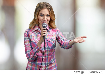 Young woman talking into microphone on abstract blurred background. 85889273