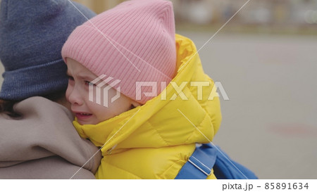 a little child with a backpack is crying in his mother's arms, tears are rolling down kid's face, little girl is upset, daughter is complaining to her mother, schoolgirl is at school with her parent a little child with a backpack is crying in his mother's arms, tears are rolling down kid's face, little girl is upset, daughter is complaining to her mother, schoolgirl is at school with her parent 85891634
