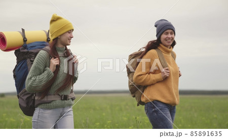 Happy girls travelers go with backpacks and smile, travel happiness, women's dream, day off in nature, long-distance hiking, sports healthy lifestyle, lovers of hiking and adventures of the 85891635