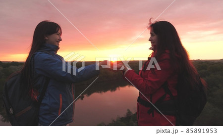 Happy female travelers stand high on the mountain and hold the sun in their hands at sunset in the sky. Women adventurers. Freedom of life on a camping trip at dawn. A good start to the day in the Happy female travelers stand high on the mountain and hold the sun in their hands at sunset in the sky. Women adventurers. Freedom of life on a camping trip at dawn. A good start to the day in the 85891953